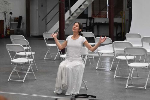 One person sitting in white in the middle of a performance space