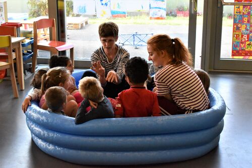 Philippa Donnellan and Olwyn Lyons sitting with children in an empty blue inflatable paddling pool