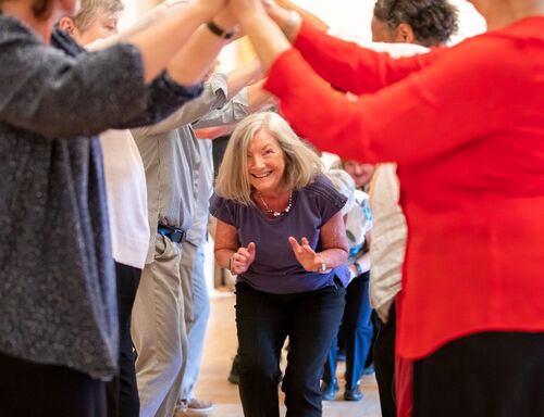 A participant laughing and ducking under an arch of others' arms