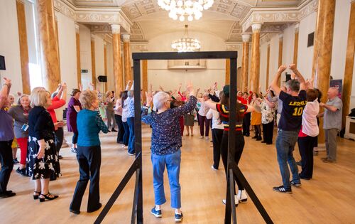 A large circle of participants facing each other seen through the frame of a black doorframe