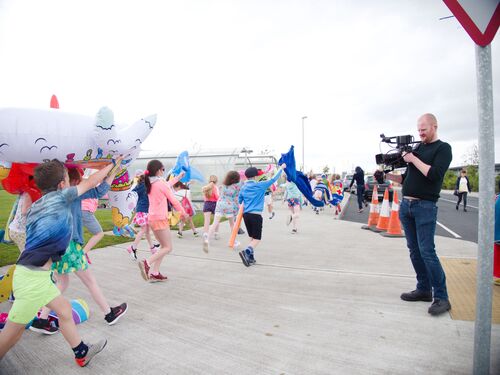 A crowd of children running past the camera with pool inflatables