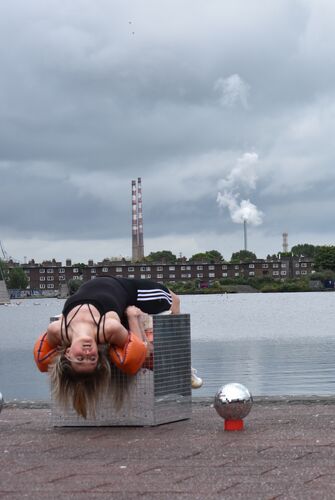 Sibéal Davitt lying back over a mirrored cube with the Poolbeg Chimneys in the distance