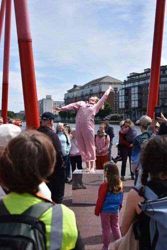 Sibéal Davitt in movement on top of a mirrored cube in the middle of a circle of audience
