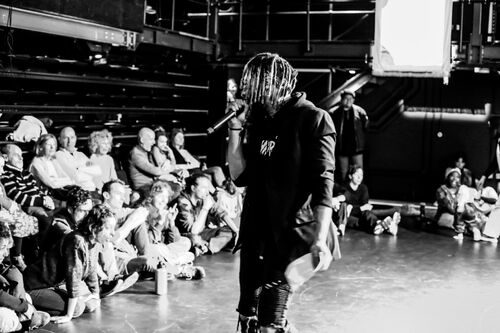 An MC with a microphone speaking to a gathered audience in black and white