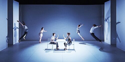 Two figures seated opposite each other centre stage with two figures in movement at either side