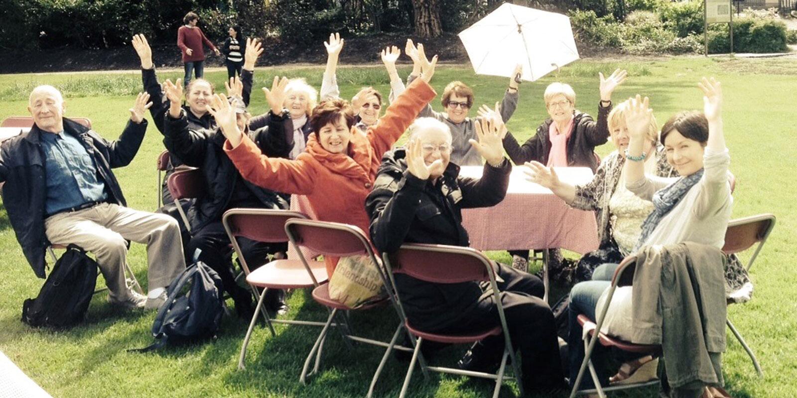 A table of participants sat outdoors with arms outstretched posing for the camera