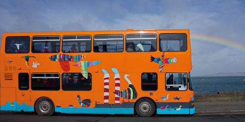 A bright orange double decker bus with illustrations printed along its side