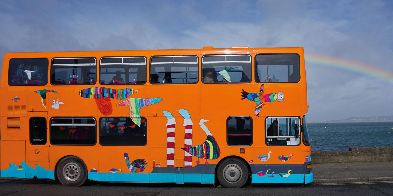 A bright orange double decker bus with illustrations printed along its side