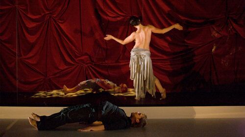 A dancer in movement with her bare back to camera with another dancer lying on the floor