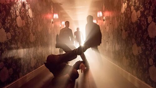 Silhouettes of four dancers in movement in a wallpapered hallway