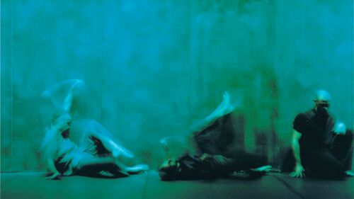 Three dancers in blurred movement on the floor cast in green light