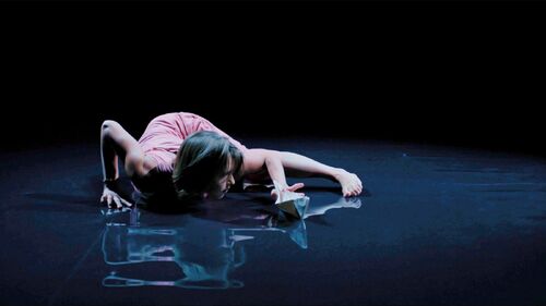 A dancer in movement on a dark reflective floor