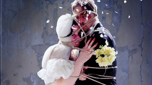 Two figures tied together facing each other with rope