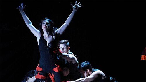 A figure with arms splayed being held aloft by other dancers