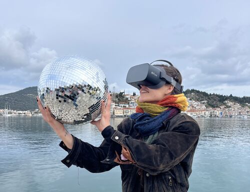 A girl in VR goggles holding a mirror ball. There is a sea and island on the background