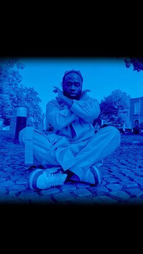 A blue filtered image of the dancer sitting on the ground in a pose with crossed legs and arms