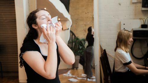 A woman leaning letters against her face, another woman in the background playing the piano