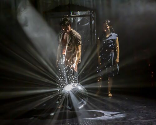 A couple of dancers on the stage looking down at the shining mirror ball