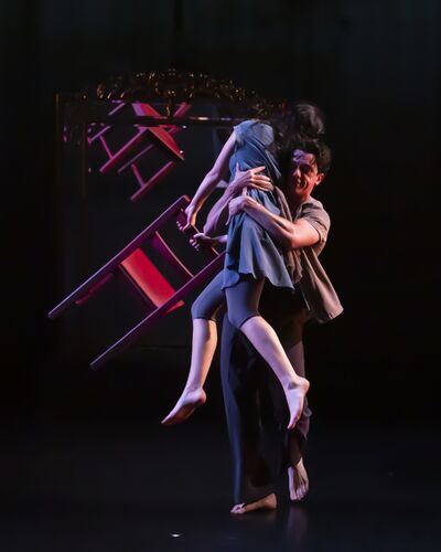 A guy holds a girl with a chair in her hands and spin her