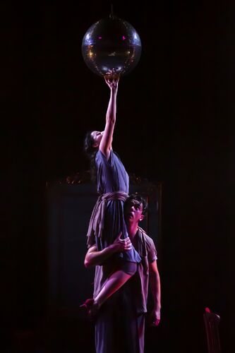 A guy has a girl on his shoulder and she is trying to reach the mirror ball