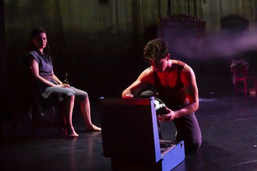 A guy knelt down and is turning on the record player. A girl in the background sitting looks at him