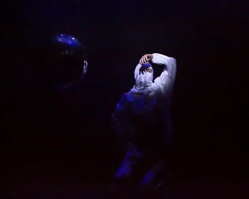 A girl in a white hazmat suit and balaclava dancing around a mirror ball