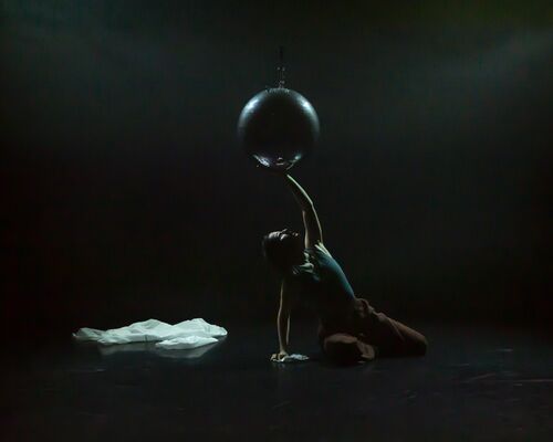 A dancer sitting under the mirror ball and touching it with her hand