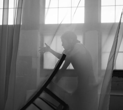 A dancer in a movement with a chair in her hand behind a transparent veil