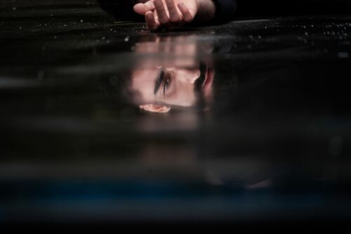 A man's face reflecting in a puddle