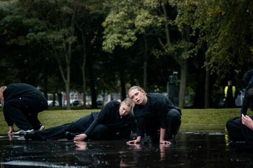 Two dancers bent over the ground with their hands on the puddles