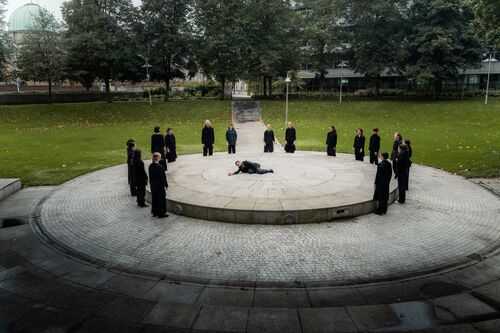 Dancers standing in a circle and a man lying on the ground in the centre
