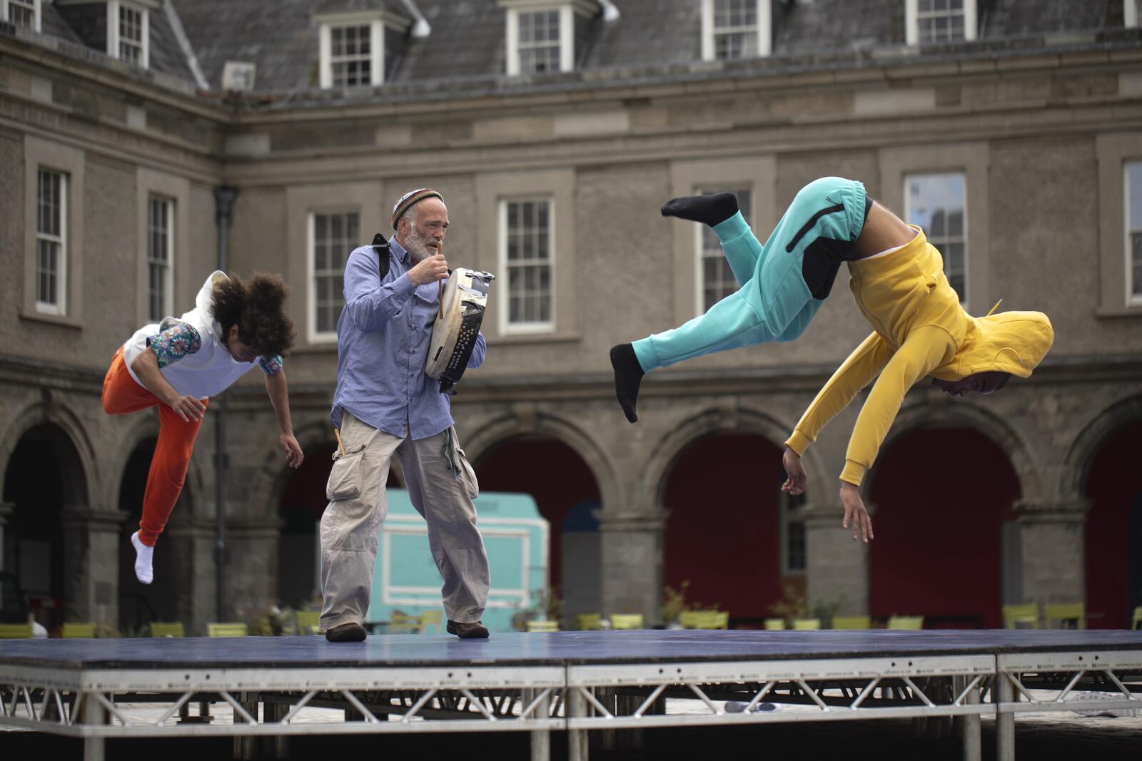 A still of two dancers breakdancing with a figure playing bodhrán between them